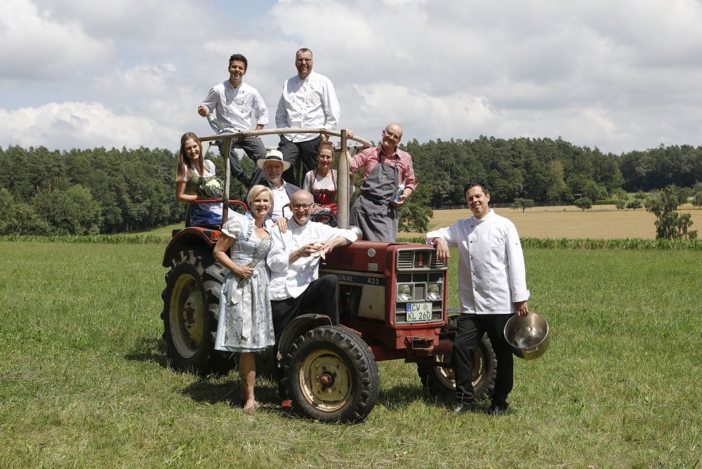 Männer und Frauen stehen und sitzen auf einem Traktor.