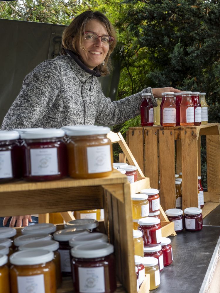 Eine Frau steht an ihrem Marktstand mit Marmeladen-Gläsern