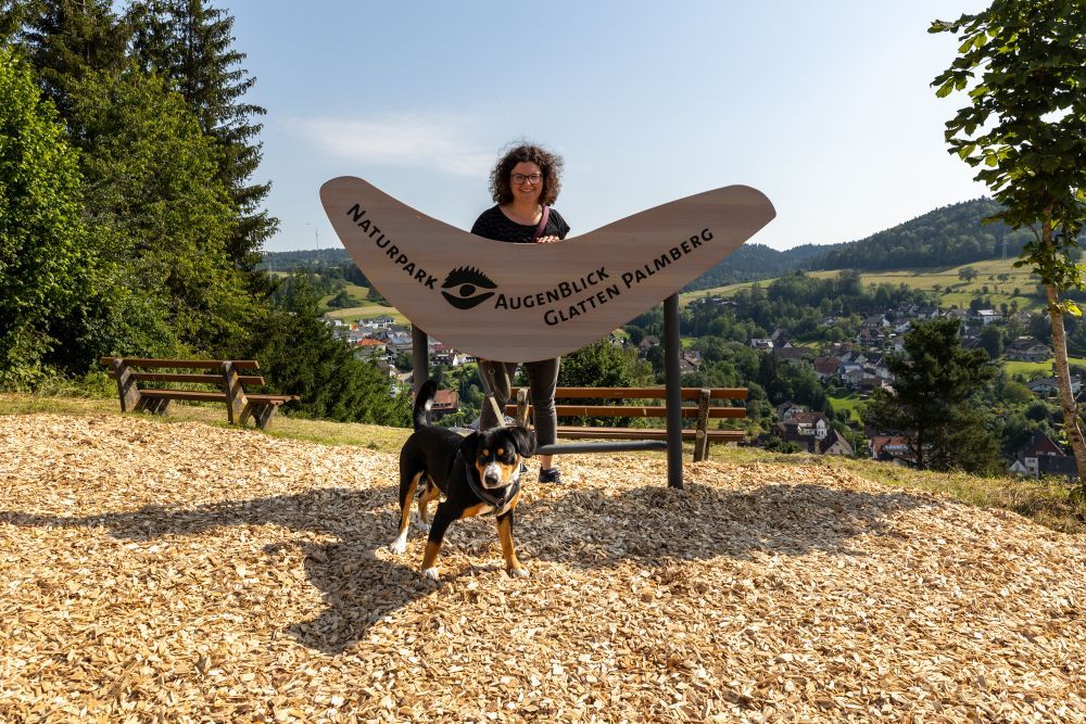 Eine junge Frau steht hinter einem Holzschild. Davor ist ein Hund zu sehen. Foto: Johannes Nickel/Naturpark Schwarzwald Mitte/Nord e. V.