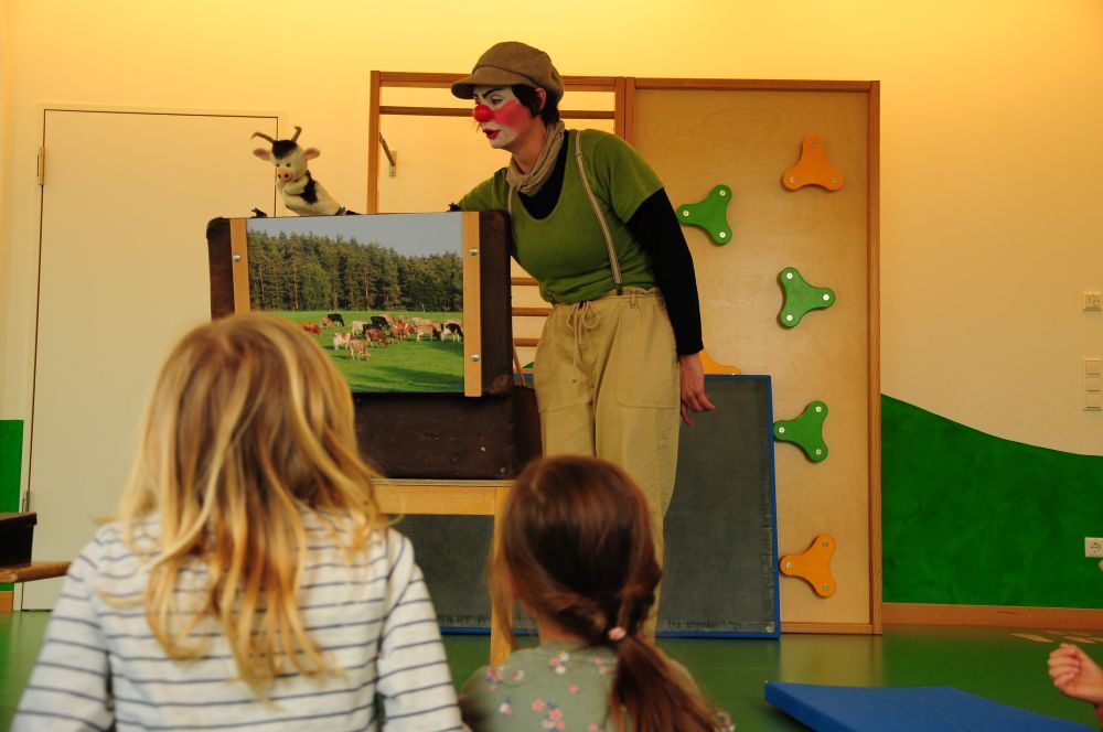 Die Clownin spielt mit der Kuh-Handpuppe etwas vor.