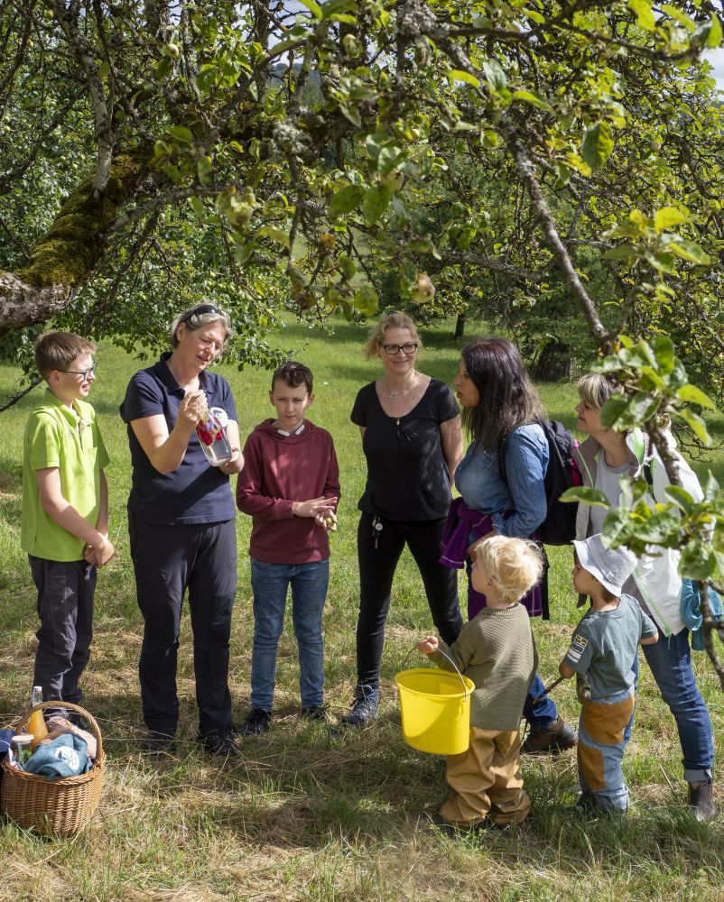 Eine Frau steht mit einer Gruppe von Menschen auf einer Streuobstwiese.