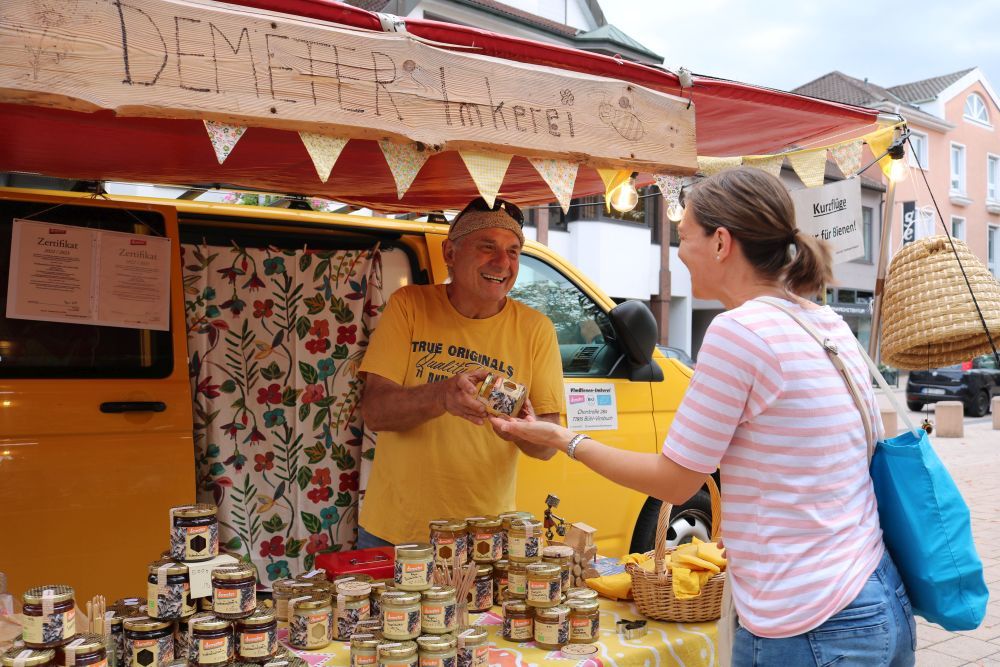 Ein Mann zeigt einer Frau an seinem Marktstand ein Honigglas.