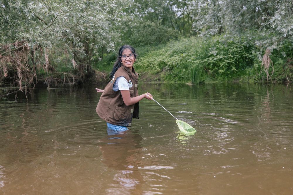 Ein Mädchen steht mit einem Kescher in einem Fluss.