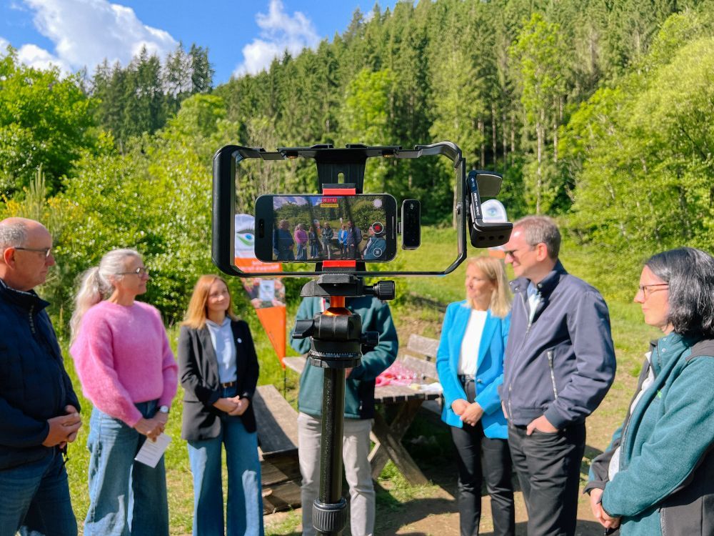 Menschen stehen bei einer Partner-Auszeichnung zusammen und werden von einer Handykamera aufgenommen.