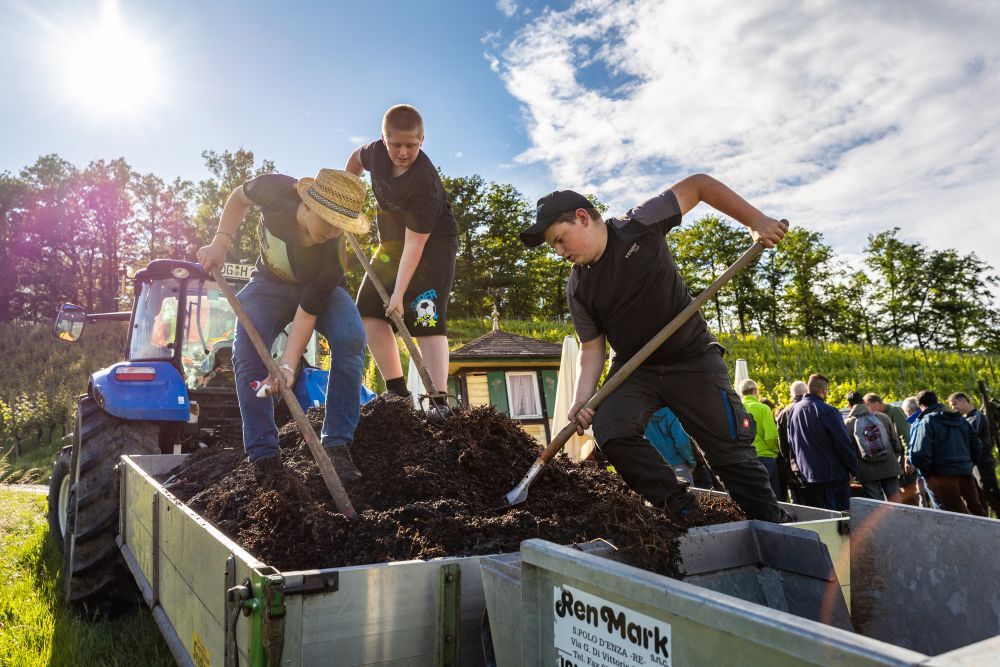 Jungs schaufeln Erde aus dem Anhänger eines Traktors.