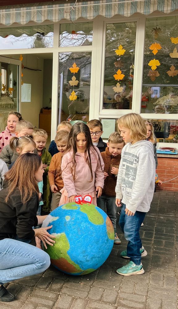 Kinder schauen Erdkugel mit Ortsmarken Naturpark, Gemeinde, Kindergarten an.