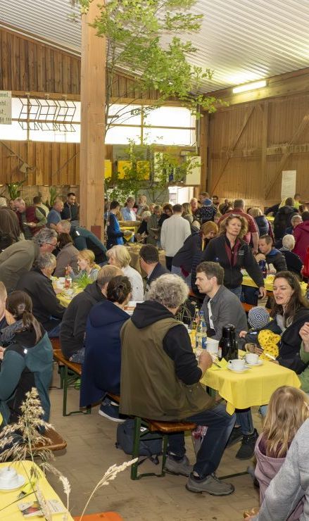 Menschen essen gemeinsam an Tischen in einer Scheune.