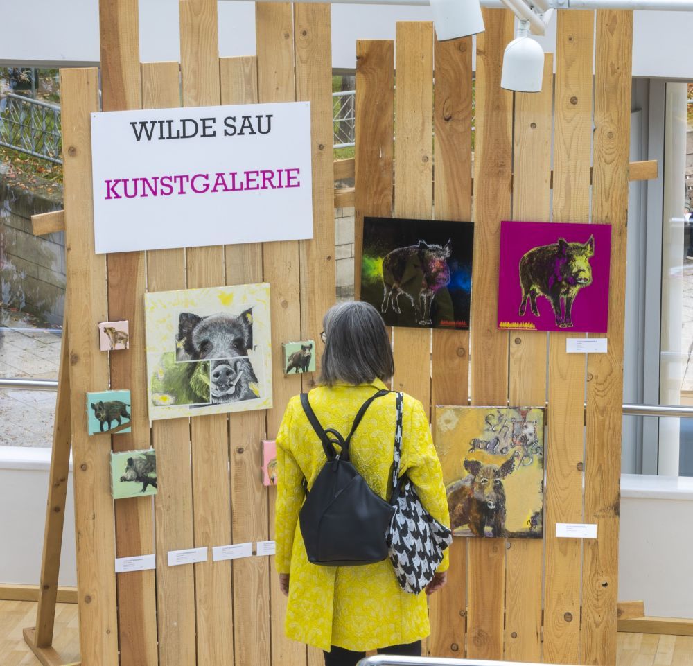 Eine Frau steht vor Gemälden, die Wildschweine zeigen.
