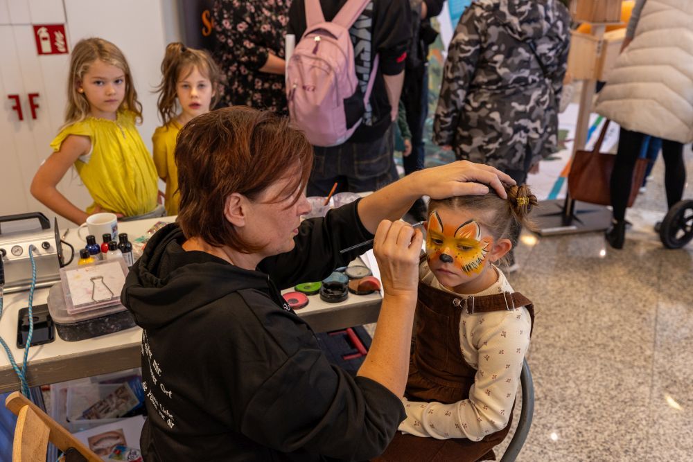 Eine Frau schminkt ein Mädchen als Wildkatze.