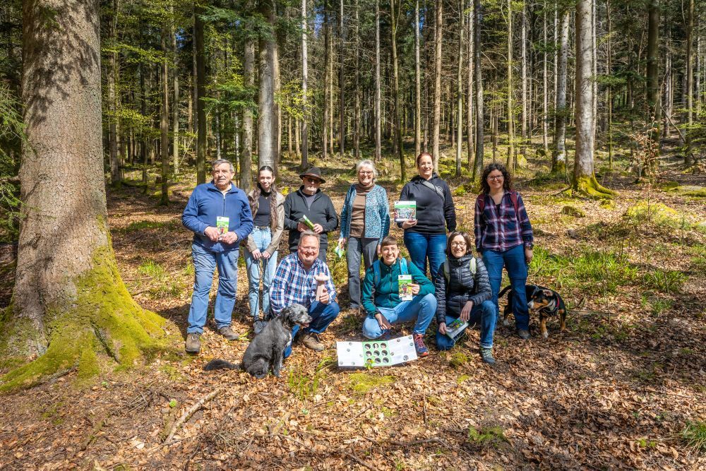 Eine Menschengruppe hat sich im Wald zu einem Gruppenbild aufgestellt.